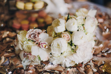 Stylish wedding bouquets with white roses,peony and orchids on table with golden confetti. Modern floral adornments