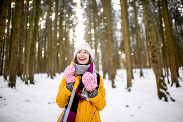 Fototapeta na wymiar Portrait of a young woman dressed in bright winter clothes standing in pine forest during the winter time