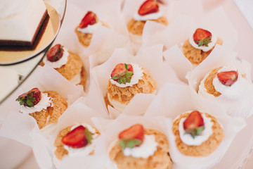 Delicious eclairs cupcakes, desserts and sweets on table party at wedding reception. White and pink stylish candy bar. Christmas and New Year feast. Celebrations and party concept.