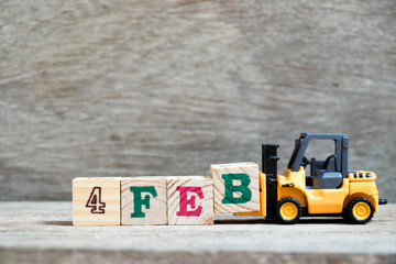 Toy forklift hold block B to complete word 4feb on wood background (Concept for calendar date 4 in month February)
