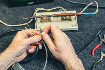 Close - up of male hand with wires and retro soldering iron. Soldering process at home