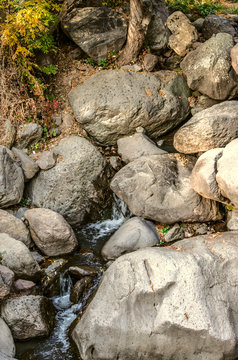 A source with foamy water littered with large stones among the yellowed grasses, flowing down into the gorge of the Geghama mountains in Armenia


