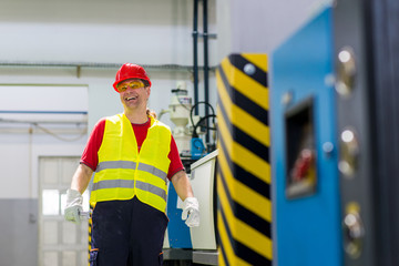 Factory worker smiling and looking at a camera standing beside a factory machine