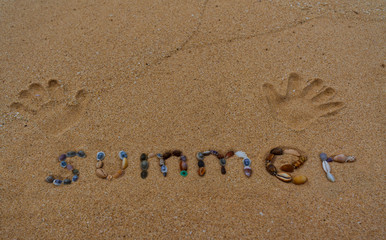Summer written on the sand with palm prints 
