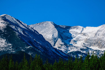 Fototapeta na wymiar Mountain snow peak, beautiful natural winter backdrop. Ice top of the hill, blue sky background. Alpine landscape, forest, tree line.