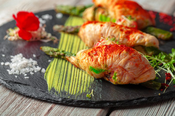 Asparagus rolled with chicken meat slices served on dark plate