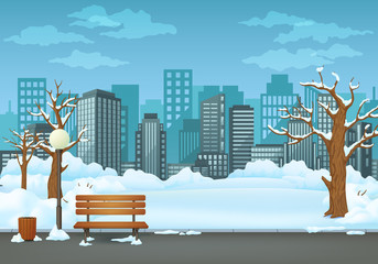 Winter day park. Snow covered wooden bench, trash bin and street lamp on an asphalt park trail with cityscape in the background.