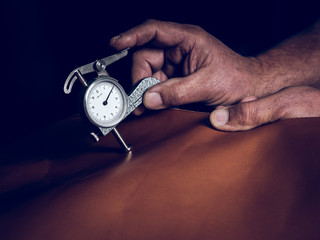 Crop hands measuring thickness of leather