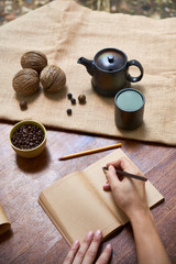 Fototapeta premium Top view of female hands making notes in notebook at the wooden table with cup of coffee