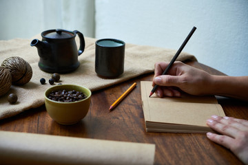 Close-up of woman opened her notebook and writing her thoughts with pencil while drinking coffee at the wooden table