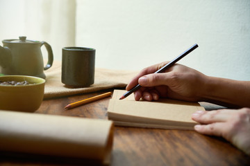 Close-up of female hands holding pencil and writing daily routine in her notebook at the table with...