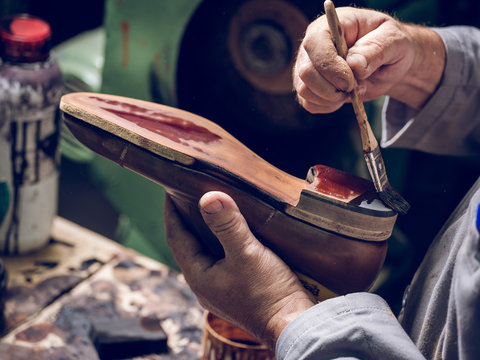 Crop shoemaker painting sole of footwear