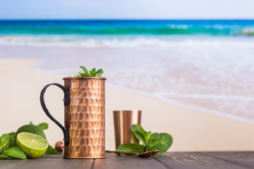 Cold Moscow Mules cocktail with ginger beer, vodka and lime over beach and seaside background