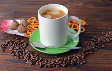 A cup of coffee on a wooden table, grains of coffee, chocolate and cookies.