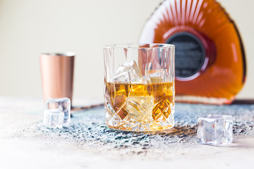 Glass of scotch whiskey with ice cubes, bottle and copper bar accessories