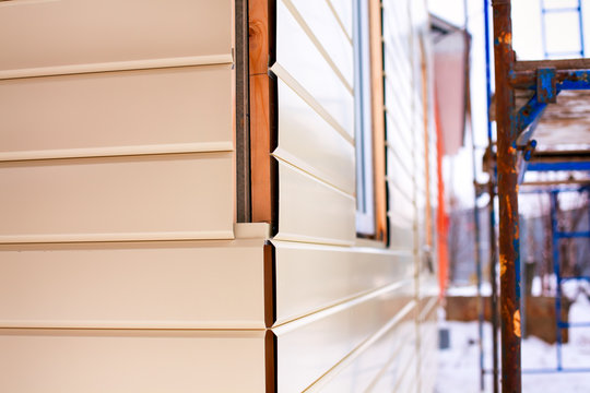 Close-up Of House Corner With Beige Siding Covering Walls And Scaffolding.