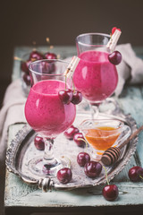 Healthy cherry smoothie with frozen strawberry, coconat water and honey in glass on white wooden table.