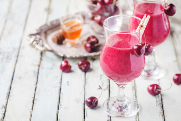 Healthy cherry smoothie with frozen strawberry, coconat water and honey in glass on white wooden table.