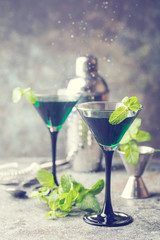 Closeup of green cocktails in martini glasses with mint leaves over gray background