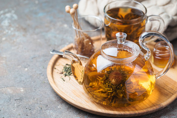 Hot green tea drink. Teapot and glass cup with blooming tea flower inside against stone background