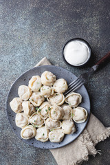 Fototapeta premium Traditional homemade Russian pelmeni meat dumplings with sour cream and greens over gray background. top view