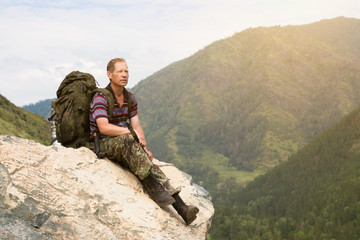 A tourist on a high mountain looks at nature. A man with a backpack sits on a large stone and looks at the landscape.