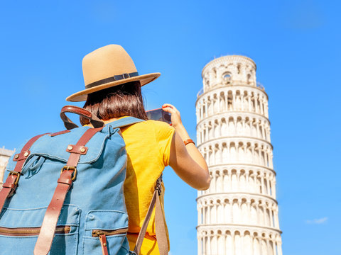 Happy female traveler in hat with backpack taking photo of the leaning tower in Pisa. Vacation and lifestyle concept