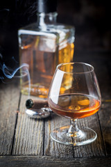 Glass and a bottle of brandy or cognac and smoking cigar on the wooden table.
