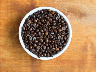 Coffee beans in white ceramic bowl on wooden table