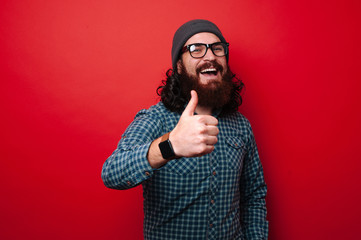 Photo of happy excited bearded man in glasses and hat showing thumb up