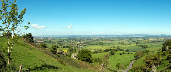 Panoramic view towards the River Severn and The Forest of Dean over a patchwork of fields with a winding road in the foreground, Coaley Peak Picnic Site and Viewpoint, Gloucestershire, UK