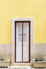 Fototapeta na wymiar A white door with red frame against yellow wall - a color contrast.