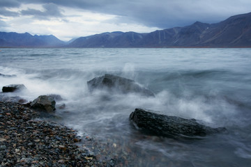 Fototapeta na wymiar Beautiful evening landscape with the bay. Waves breaking on the rocks. Mountains at dusk. Gloomy autumn weather. Egvekinot, Kresta Bay, Bering Sea, Chukotka, Far East of Russia. Perfect for background