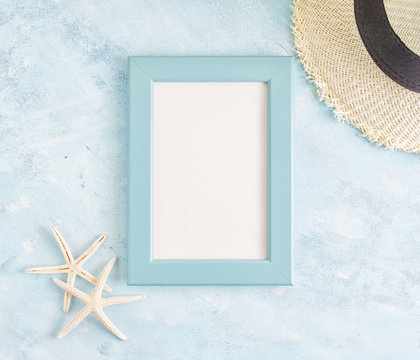 Top view flat lay summer mockup: empty blue photo frame, straw hat and starfish on blue background. Vacation concept. Space for lettering