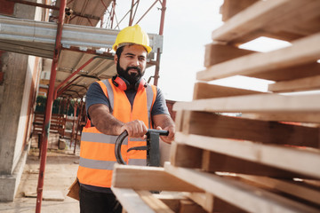 Latino Manual Worker With Forkift Pallet Stacker In Construction Site - obrazy, fototapety, plakaty
