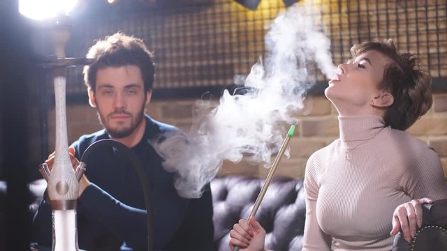 Beautiful blond woman smoking while sitting with friends. Attractive fair-haired girl smoking flavored tobacco