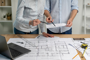 Cropped collaboration of two builder person analyzing inspect paper paperwork stand in formalwear shirt in bright loft interior workstation read civil sketch put measurement divider pencil on desk