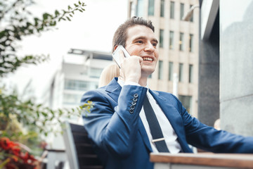 Young businessman talking by mobile phone in street cafe and looking straight.