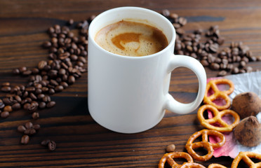 A cup of coffee on a wooden table, grains of coffee, chocolate and cookies.