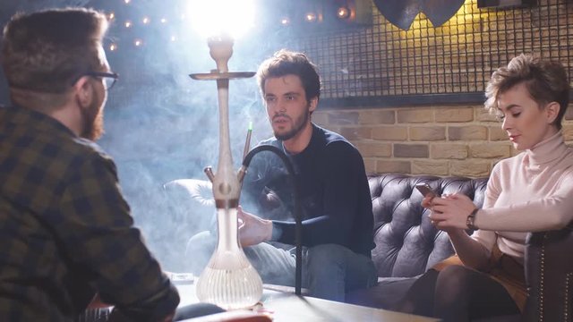 Group of young cheerful friends relaxing in shisha club. Entertainment. Time with best friends