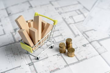 High and low price concept. High angle above top view small miniature object of shopping cart full of sawmill construction materials standing on table with stack of gold coins indoor light room