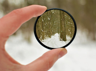 Hand holds a circular polarizer filter on winter landscape background. Winter season....