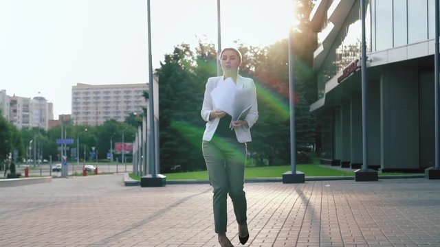 Business woman in heels walks down the street, stumbles, drops documents, and puts them in order. Fail. Sunrise. Slow motion