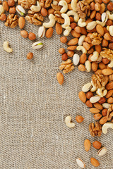 Mix of nuts of cashew, almonds, pistachios, hazelnuts and walnuts is against the background of brown fabric of burlap. Nuts as structure and background, macro