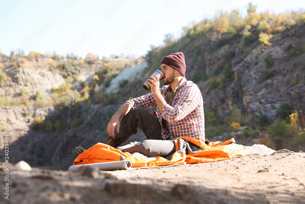 Sticker male camper with thermos sitting on sleeping bag in wilderness