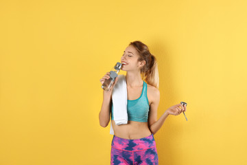 Beautiful young woman in sportswear with towel and bottle of water on color background
