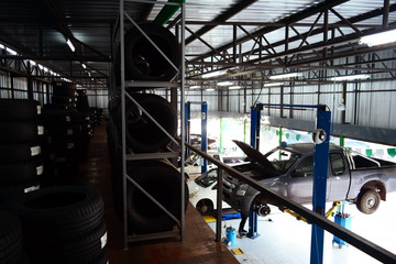 Obraz na płótnie Canvas the grey pick up car and other car at service bay inside the car service center with the many tyres on shelf at above and blue oil tank at bottom with bright daylight from outside
