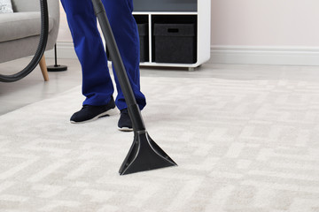 Man removing dirt from carpet with vacuum cleaner indoors, closeup. Space for text