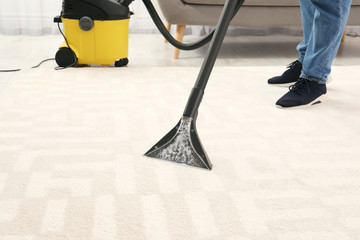 Man removing dirt from carpet with vacuum cleaner indoors, closeup