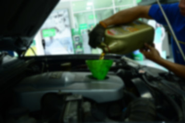 the blur of  mechanic in blue uniform refilling the engine oil into the engine at service bay inside the car service center